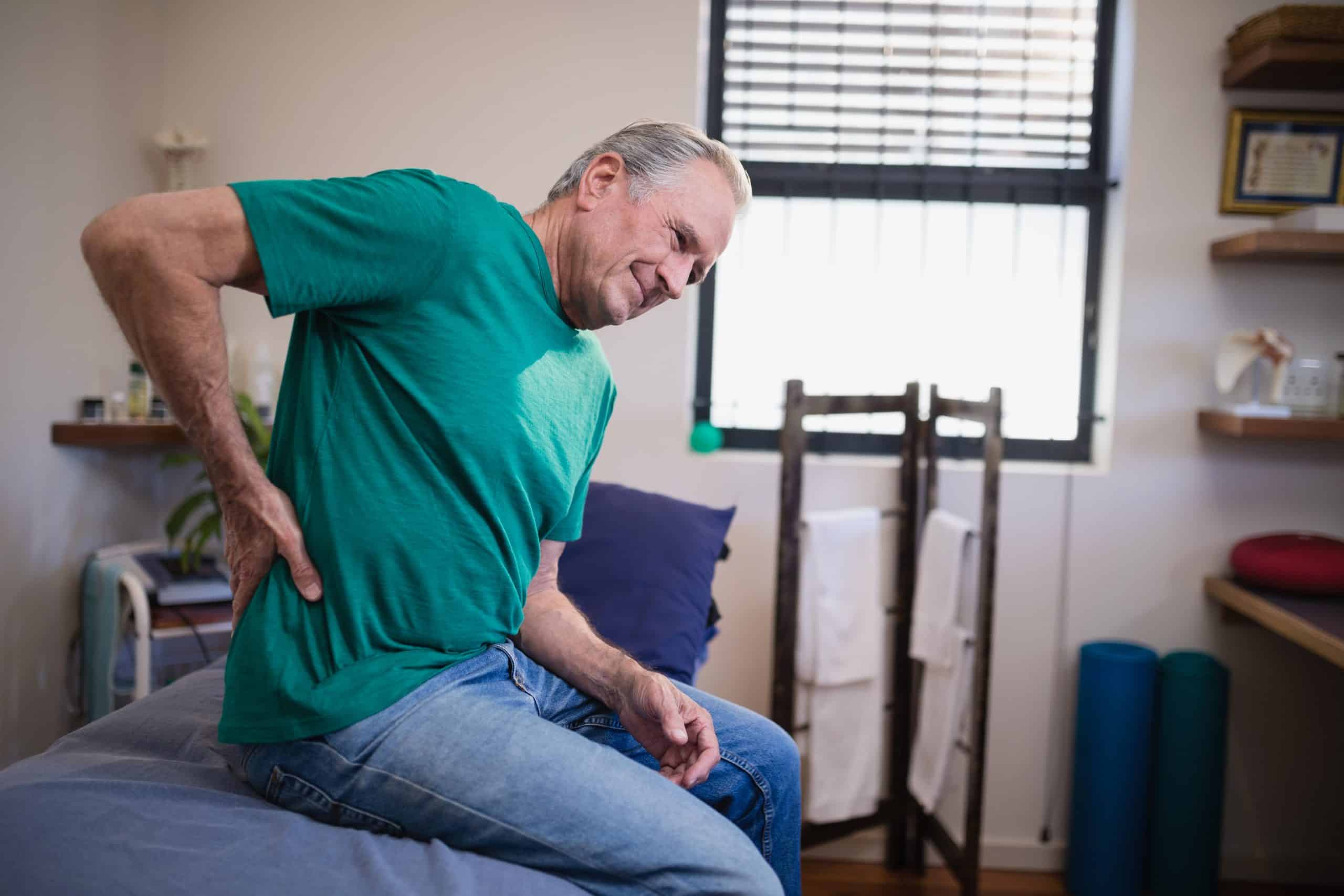 Side view of male patient suffering from back ache while sitting on bed