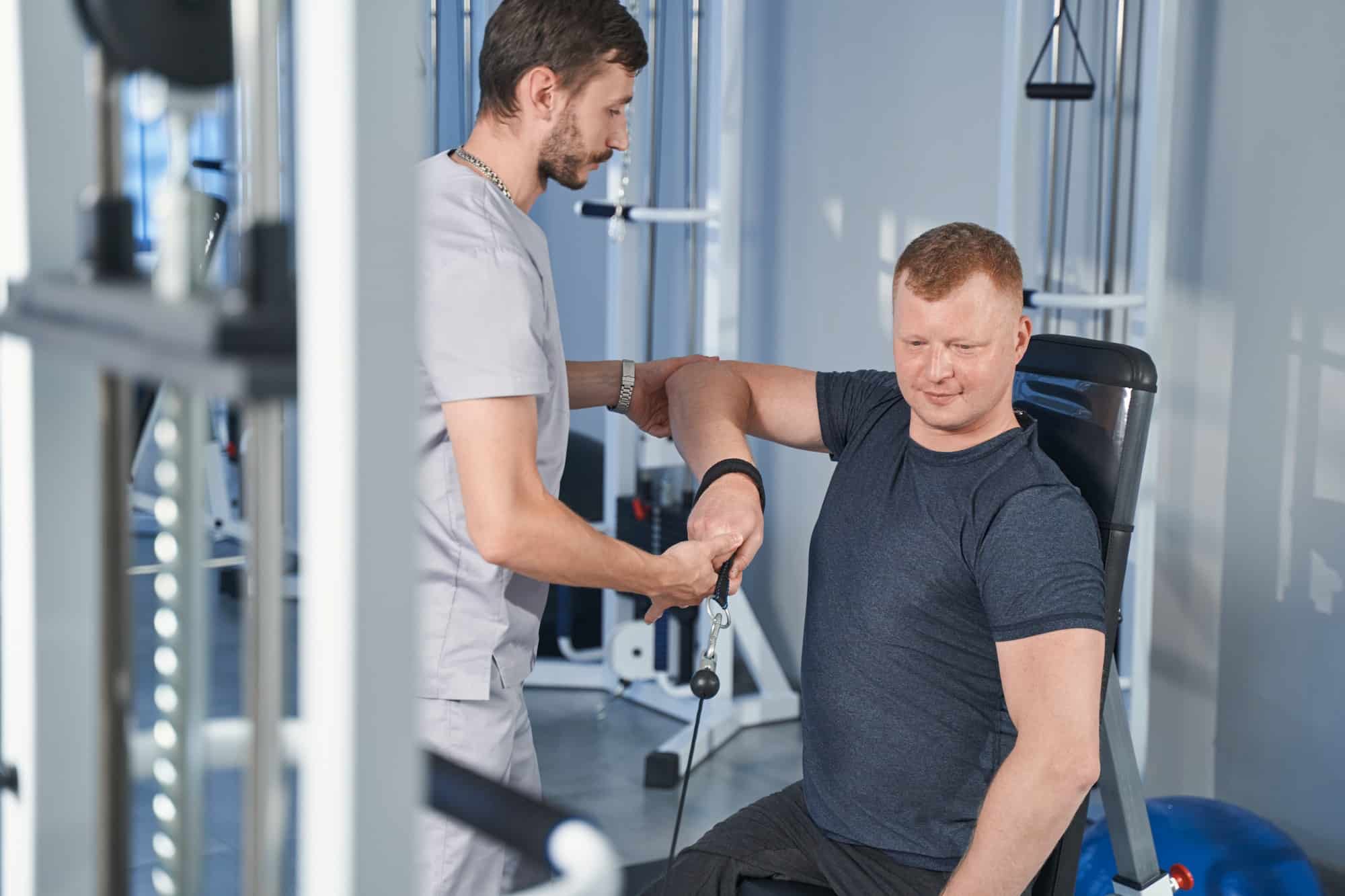 Physician helps man with disability lift arm on rehab weight simulator